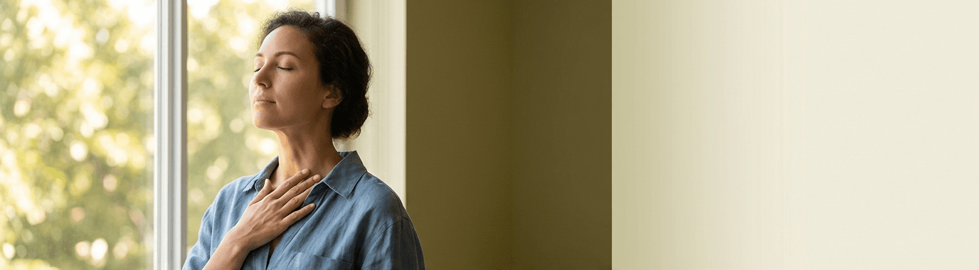 אישה שמשדרת נינוחות עם עיניים עצומות, על רקע נוף הנשקף מחלונה, ומחזיקה את ידה בעדינות מתחת לצווארה.